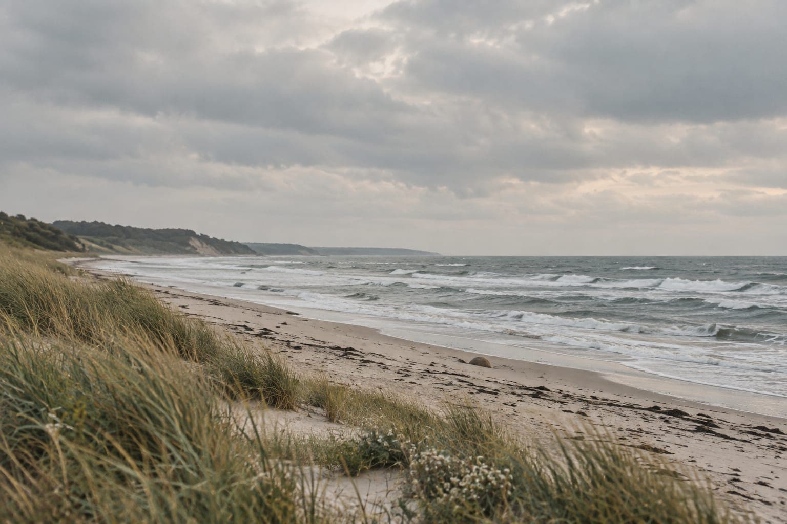 Waves rolling onto a beach with dune grass under a cloudy sky – inner restlessness and how to relate to it